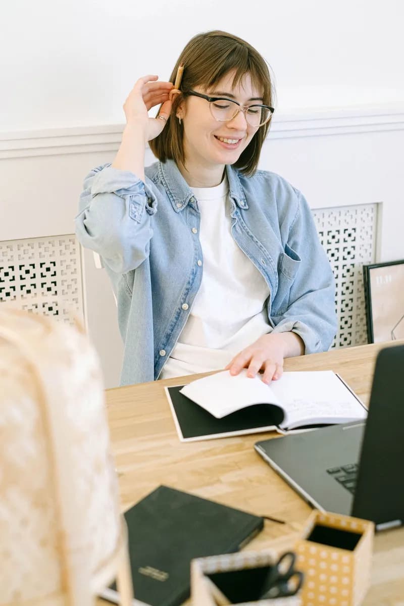 Smiling woman in casual attire working at home office with a laptop and notebook
