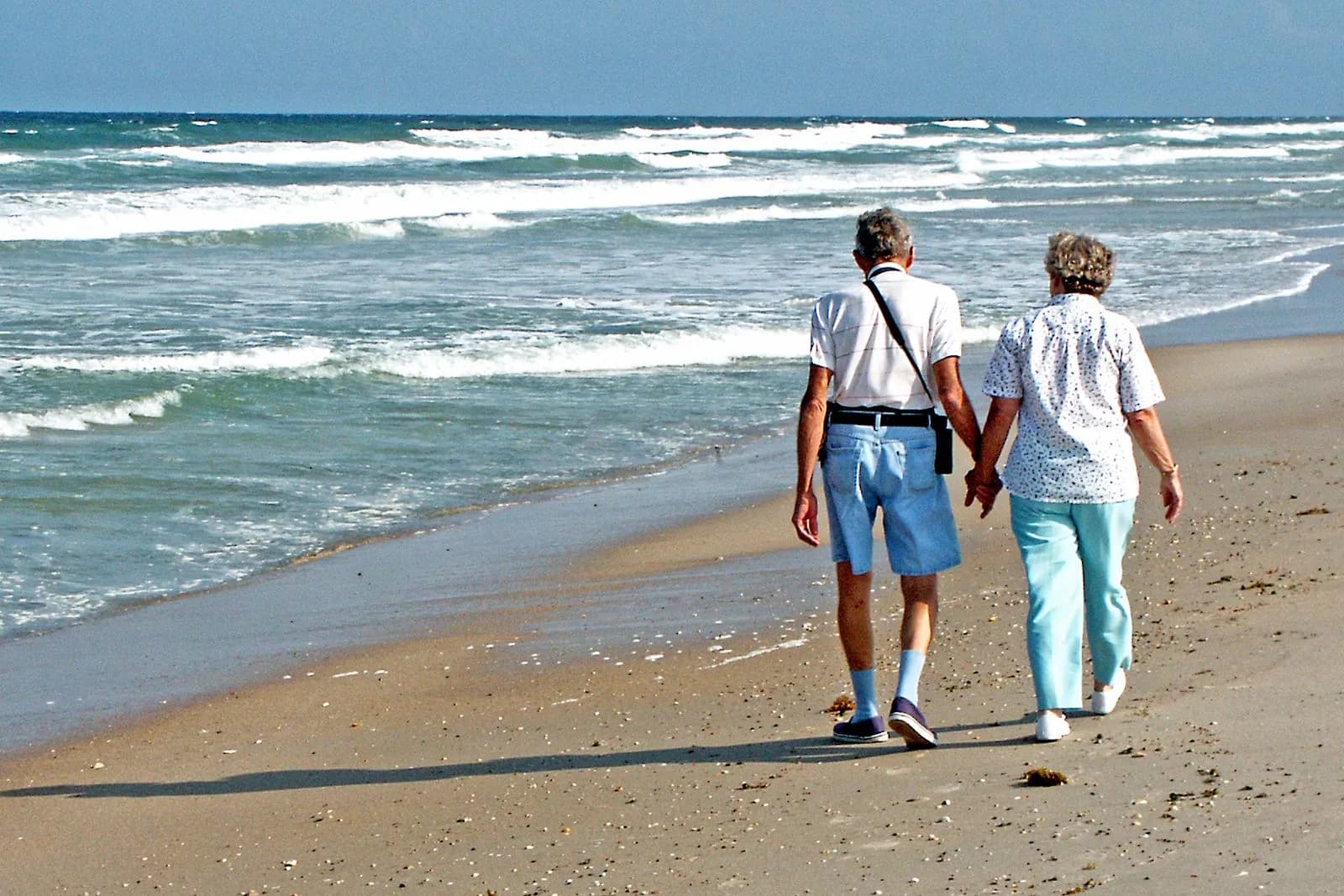 A senior couple enjoys a peaceful walk along the sunny Florida beach, hand in hand.
