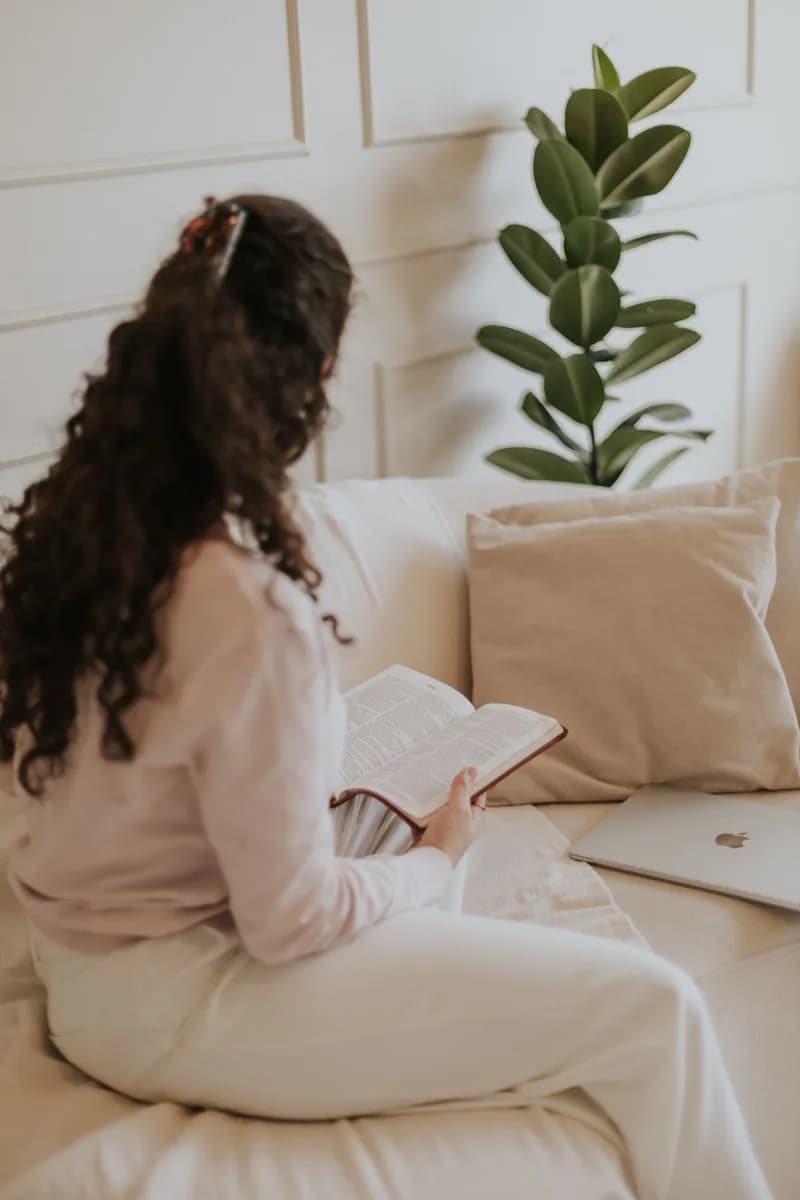 A woman reading on a sofa beside her laptop