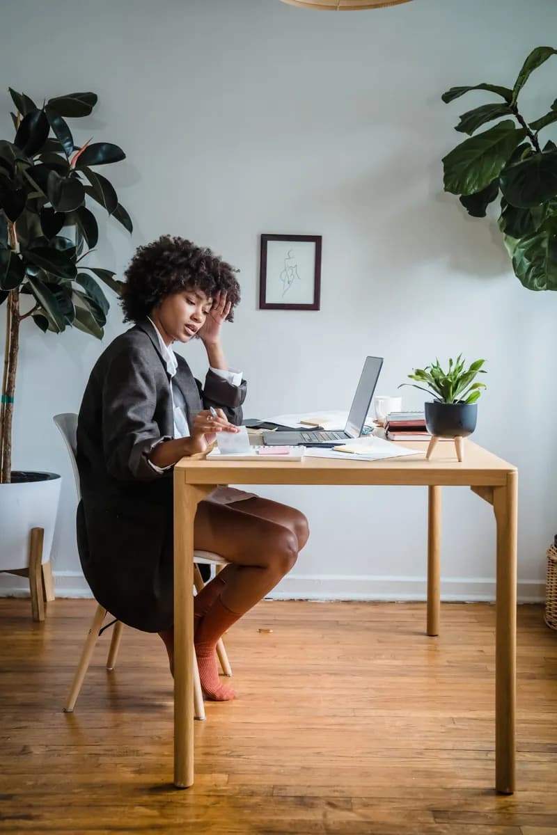 Woman with curly hair working on a laptop in a modern home office with plants