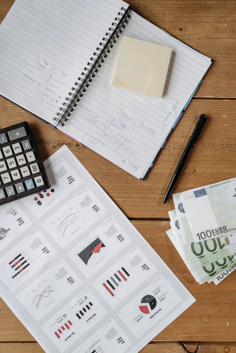 High-angle view of a financial workspace with charts, Euro bills, calculator, and notebook on a wooden desk