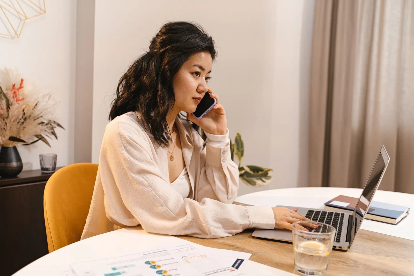 Adult woman working from home, using a laptop and mobile phone at a home office desk.