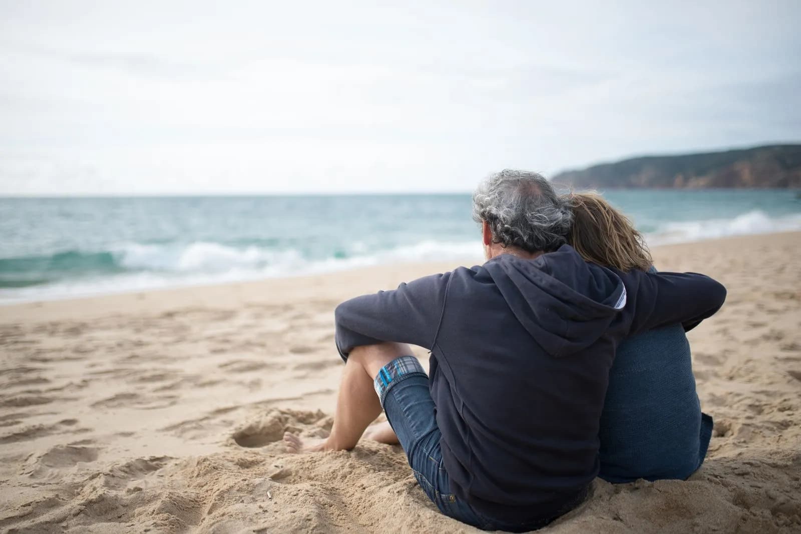 An affectionate senior couple sits together on a sandy beach, enjoying a peaceful moment by the ocean.