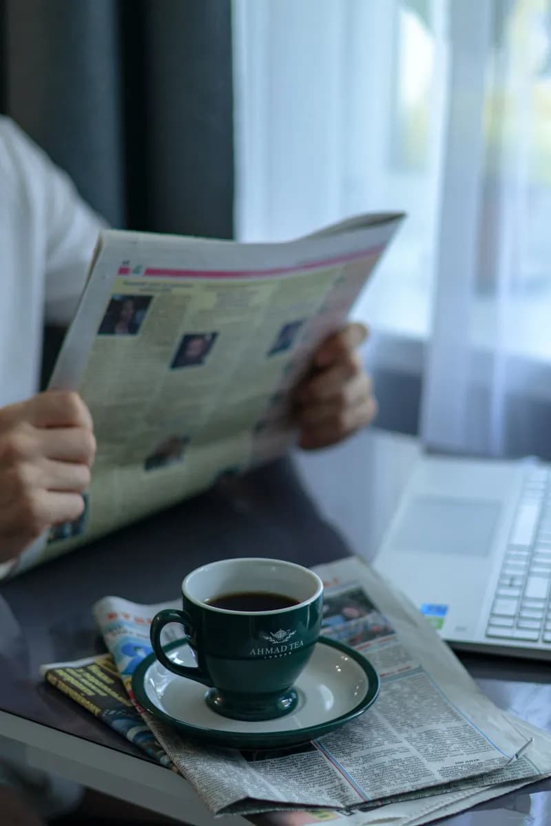 Man reading newspaper with a cup of coffee at a desk, creating a calm morning routine atmosphere.