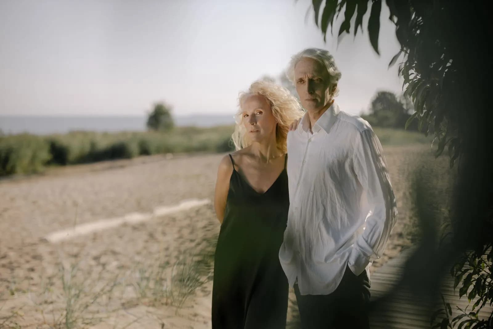 An older couple standing together beside a sunlit coastal path