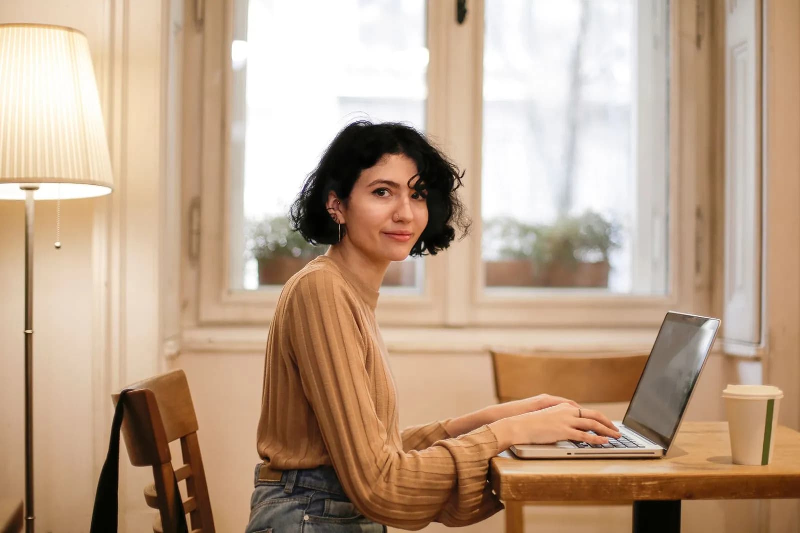 A woman smiling while working on a laptop at home, highlighting remote work and comfort.